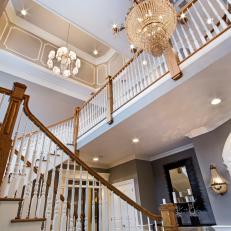 Tall, Open Multi-Floor Foyer With Decorative Chandelier and Wood Columns Lining the Staircase 