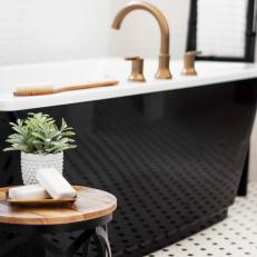 Black Soaking Tub in Bathroom with Black-and-White Floor and Nearby Table, Towels and Accessories