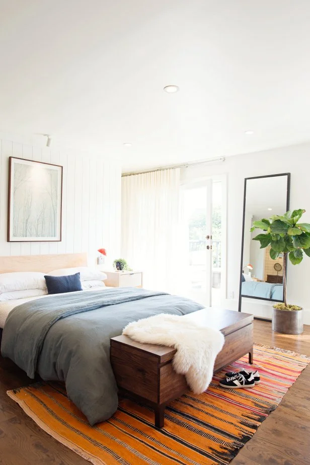 White Bedroom With Orange Rug, Wood Chest and Potted Tree