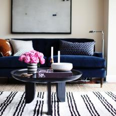 Chic, Midcentury Modern Living Area Features Navy Sofa & Striped Rug