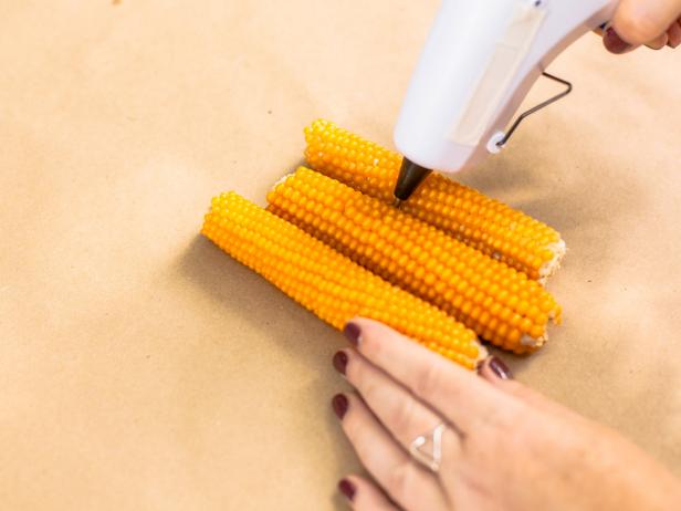Lay the three corn cobs side by side, staggering their heights a bit. Hold them tightly together as you hot glue them into place.