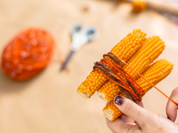 Wrap the corn cobs in wire and yarn and tie off, then secure with hot glue. Use the grapevine wire to attach this to the base of wreath, a bit off center.