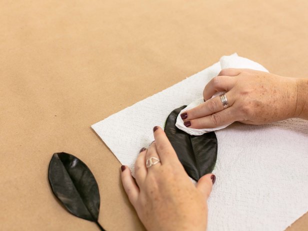 Use a paper towel to gently remove some of the preservative from the magnolia leaves. Then, using acrylic craft paints in metallic colors, lightly paint leaves in an imperfect way to give them a rustic look. After the leaves have fully dried, fasten a 9-12 inch length of sheer ribbon or yarn to the stem of each leaf, securing with brown floral tape. Add a dab of hot glue, as well for extra strength. Set leaves aside when done.