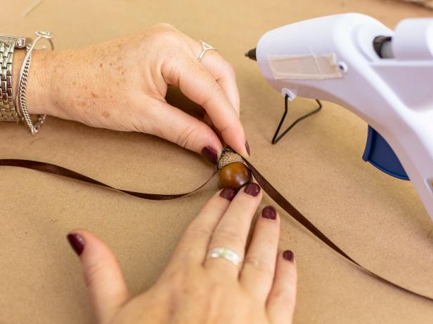 Cut a 9 inch piece of satin ribbon and fold in half. Place a dab of hot glue directly onto the acorn cap and attach ribbon at the fold. Press gently and let cool. Set acorns aside.