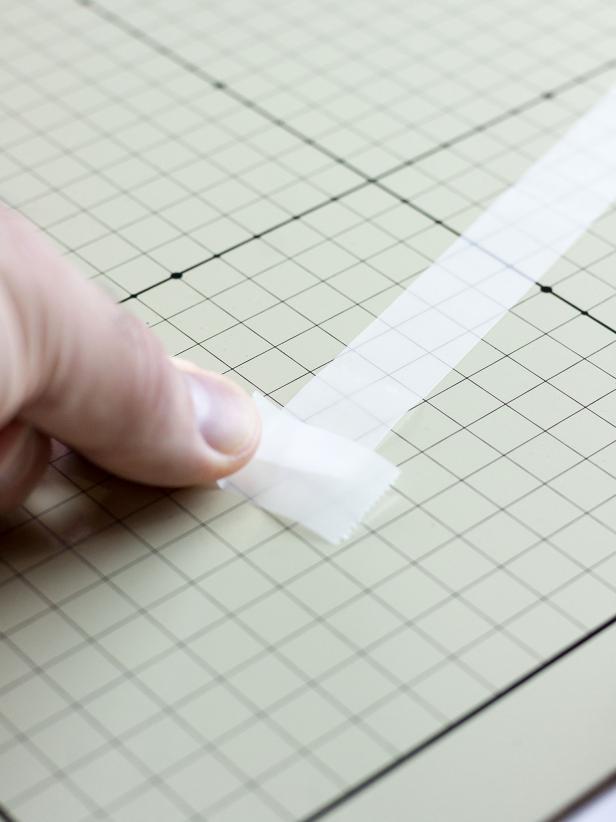 Lay a 9 inch piece of clear tape adhesive-side-up on a flat work surface. Tear off smaller pieces of tape and tape the upside-down piece to the work surface on both ends.