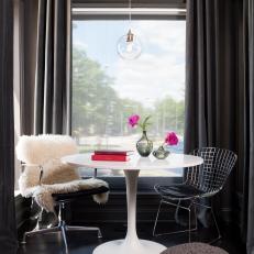 Window Nook With Black Accordion Curtains, Fur-Draped Chair and Globe Pendant Over White Table 