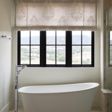 Bathroom Features Freestanding Bathtub, Marble Floors & Neutral Roman Shade