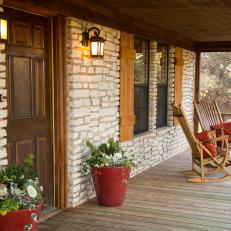 Natural Stone and Wood Covered Front Porch With Wood Rocking Chairs, Sconce Lighting and Potted Plants