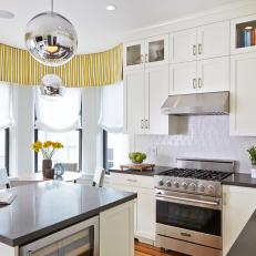 White Cabinetry and Patterned White Backsplash in Bright Transitional Kitchen With Yellow Striped Valance and Silver Globe Pendants