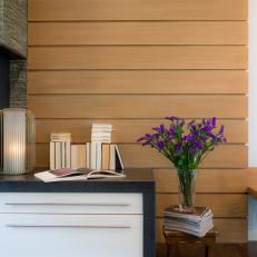 Wood Panel Wall Decor Behind Contemporary Dresser With Black Stone Top, Stacked Book Display and Purple Flowers for Color