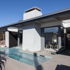 Modern Swimming Pool and Gray Tile Patio Outside Modern Home With White Brick Exterior Elements 