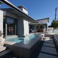 Modern Backyard With L-Shaped Swimming Pool, Concrete Tile Walkway and Gray Cushioned Seating With Striped Throw Pillows 