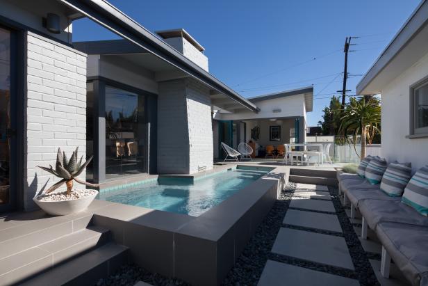 Modern Backyard With L-Shaped Swimming Pool, Concrete Tile Walkway and Gray Cushioned Seating With Striped Throw Pillows 
