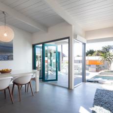 Bright, Open Dining Room With White Exposed Beams, Dining Table and Bucket Chairs and Turquoise Accordion Door
