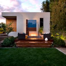 Backyard of a Modern White Home Featuring Wood Deck, Lush Lawn and Fireplace
