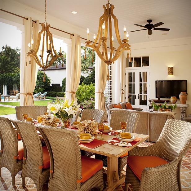 A covered pavilion with herringbone brick floors creates a nice spot for dining al fresco in view of the pool. Peppy orange fabrics bring life to the woven indoor-outdoor seating, while unique wood chandeliers and a wall-mounted TV bring the indoors out.