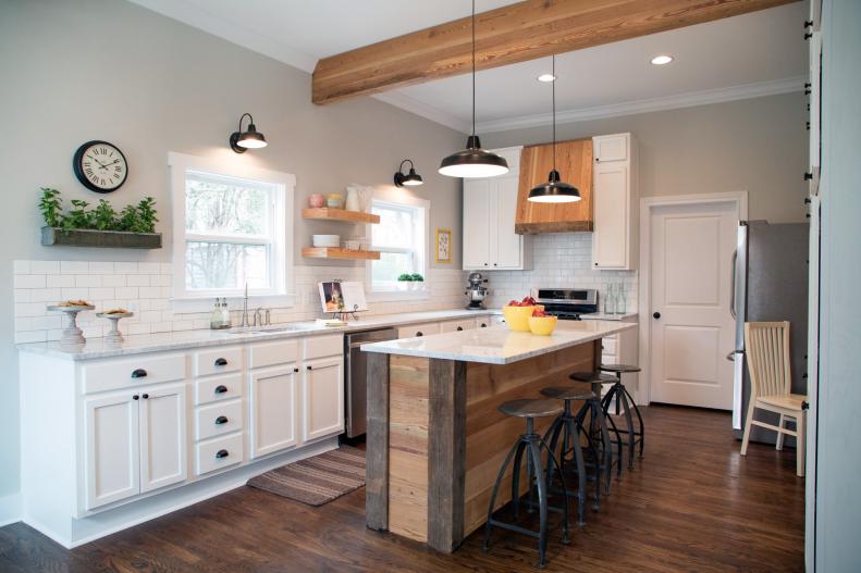 Fixer Upper Hosts Chip and Joanna Gaines turned the once disastrous room into a bright, clean kitchen with new cabinets, wood floors, Carrera marble countertops and light gray paint with white trim.  The old drop ceiling was removed, adding height to the room, and a wooden support beam was added.  A subway tile backsplash, floating wood shelves, and stainless steel appliances were also installed. Client Clint Harper added the finishing touches to the kitchen by making a beautiful island and vent hood out of reclaimed wood , as seen on HGTV's Fixer Upper.  (After 7a)  Afters