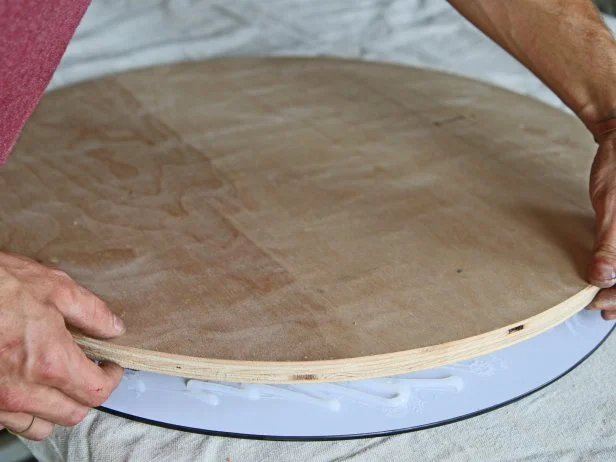Place the round plywood cutout on top of the silicone on the back of the mirror, and press down lightly