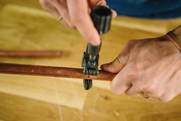 Cut copper piping using a pipe cutter.