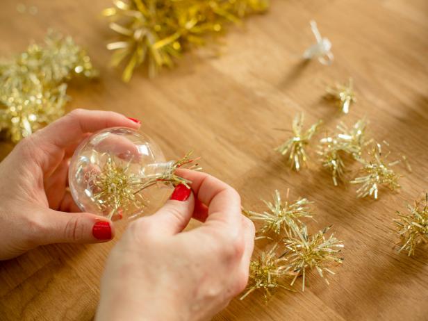 Remove the tops of the ornaments and pop pieces of tinsel inside. You;ll want to place several pieces into each ornament to get a full effect, then replace the top . HINT: a dab of hot glue should keep the tops in place if they're prone to popping off.