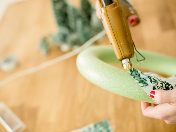 Dab a bit of hot glue onto the back of wreath and secure the edge of fabric to foam.  Then, begin wrapping the fabric strips around the wreath. Repeat, securing with hot glue periodically, until the foam wreath is completely covered by fabric.