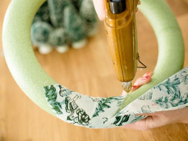 Dab a bit of hot glue onto the back of wreath and secure the edge of fabric to foam. Then, begin wrapping the fabric strips around the wreath. Repeat, securing with hot glue periodically, until the foam wreath is completely covered by fabric.