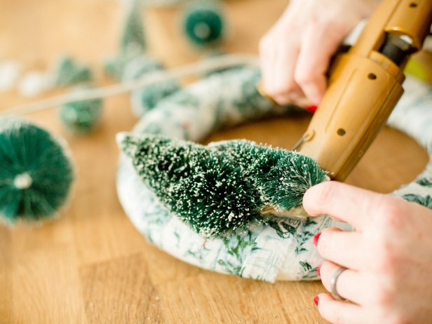 Remove the bases of the bottle brush trees and bushes so that the wire is exposed. Insert wire into the foam wreath, then bend so that the tree is flat against wreath, securing with hot glue as needed. Repeat with other trees and bushes until you get a landscape effect on either side of the wreath.