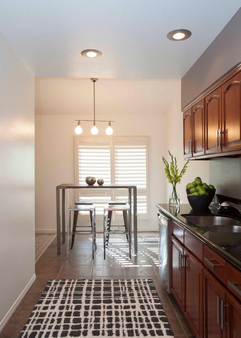 As seen on HGTV's House Hunters Renovation, the open floor plan of Josh Campbell and Mac Gaspard's Studio City, California, townhouse reflects the couple's desire for a loft-style home with lots of light and a minimalistic design aesthetic. An industrial-style bar table and four stools create an intimate dining space for the couple just off of the kitchen on the second floor, while a grey accent wall and new silver hardware on the cabinets freshened the space. (After IMG_4251)