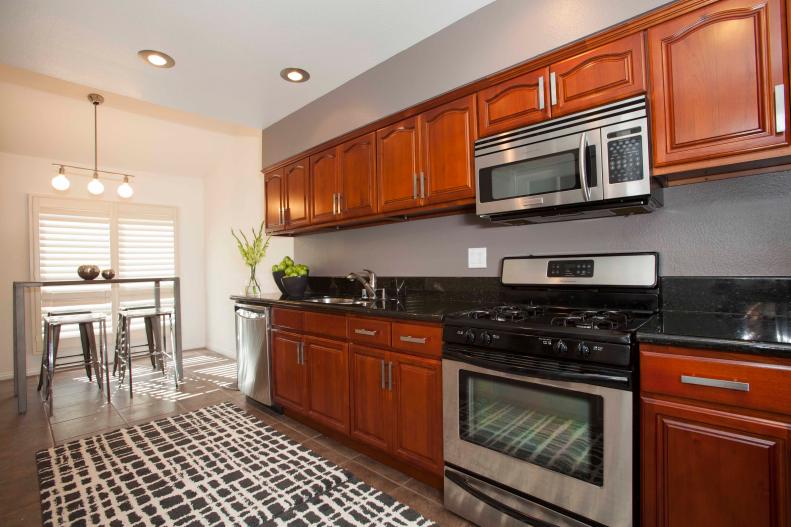 As seen on HGTV's House Hunters Renovation, the open floor plan of Josh Campbell and Mac Gaspard's Studio City, California, townhouse reflects the couple's desire for a loft-style home with lots of light and a minimalistic design aesthetic. An industrial-style bar table and four stools create an intimate dining space for the couple just off of the kitchen on the second floor, while a grey accent wall and new silver hardware on the cabinets freshened the space. (After)