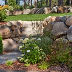 Rock Landscaping in Yard With Stone Steps Leading From Lush Grass to Concrete Driveway 
