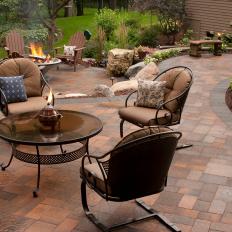 Outdoor Sitting Area on Paver Patio With Neutral Tufted Cushions on Wrought Iron Chairs Around a Glass Circular Table