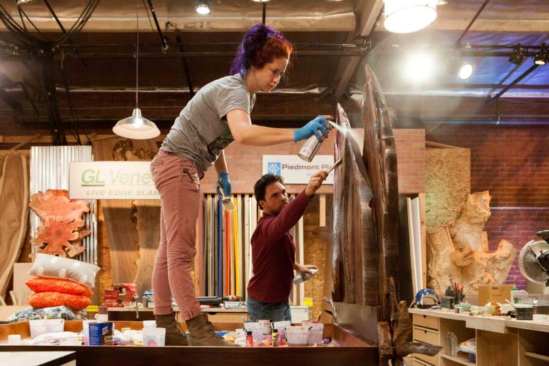 Designer Mckenzie Gibsons adds a later of spray adhesive as carpenter Brooks Utley paints the finishing touch on the bed's head board as seen on Ellen's Design Challenge.