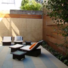 Asian Outdoor Sitting Room With Striped Patio Floor, Black Furniture With White Cushioning and Textured Retaining Walls 