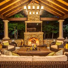 Outdoor Living Room With Stone Fireplace and Chimney, Wicker Furniture and Green Accent Throw Pillows 