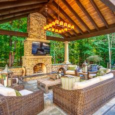 Wicker Furniture With Green Accent Pillows and Stone Fireplace and Chimney in Neutral Outdoor Living Room 