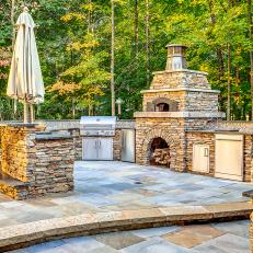 Natural Stone Outdoor Kitchen Featuring Pizza Oven, Stainless Steel Grill and Bar Seating 