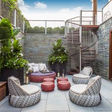 Lower Level Outdoor Living Room With Circular Weaved Furniture, Large Planters and Spiral Staircase Access