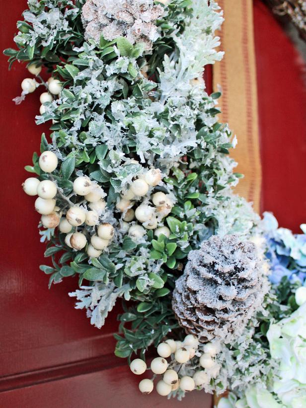 Add faux greenery, flowers, berry sprigs and glittered pinecones to a grapevine wreath then cover with faux snow to give your front door a cheery update during winter months.