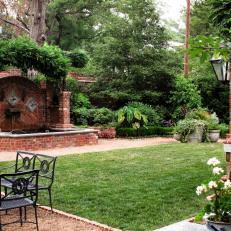 Whimsical Garden With Brick Water Fountain Structure, Gravel and Concrete Yard Frame and Black Wrought Iron Seating