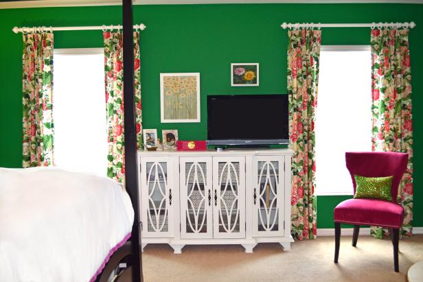 Green bedroom with floral curtains, white sideboard, and a pink chair.