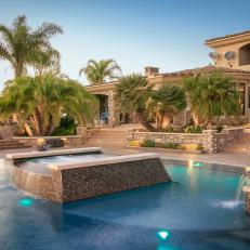 Dreamy Backyard Swimming Pool With In-Pool Waterfalls, Groupings of Palm Trees and Stone Walls 