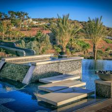 Modern Swimming Pool Details With a Tropical Vibe Featuring A Pathway Over the Water and In-Pool Water Feature