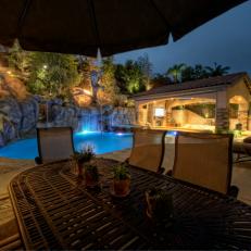 Outdoor Dining Table Sits Next to An Amazing Pool with Waterfall, Water Slide, Rope Swing, and Faux Burning Trees