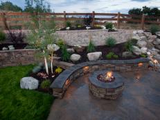 A backyard fire pit is set under flowing lines of rising stone walls