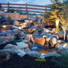 A Water Feature Surrounded By Natural Stone Gives Depth To A Backyard Landscape