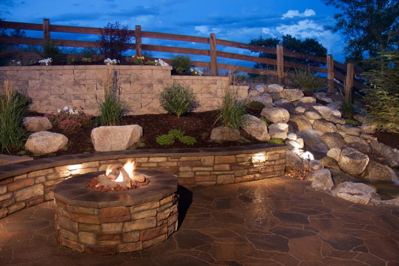 The flames of a stone fire pit adds warmth to a stone-walled backyard