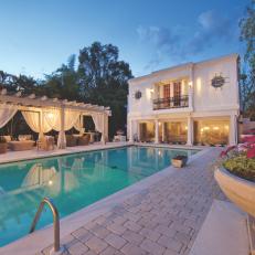 Elegant Swimming Pool With Pergola Covered Lounge Cabana and Illuminated Home Exterior