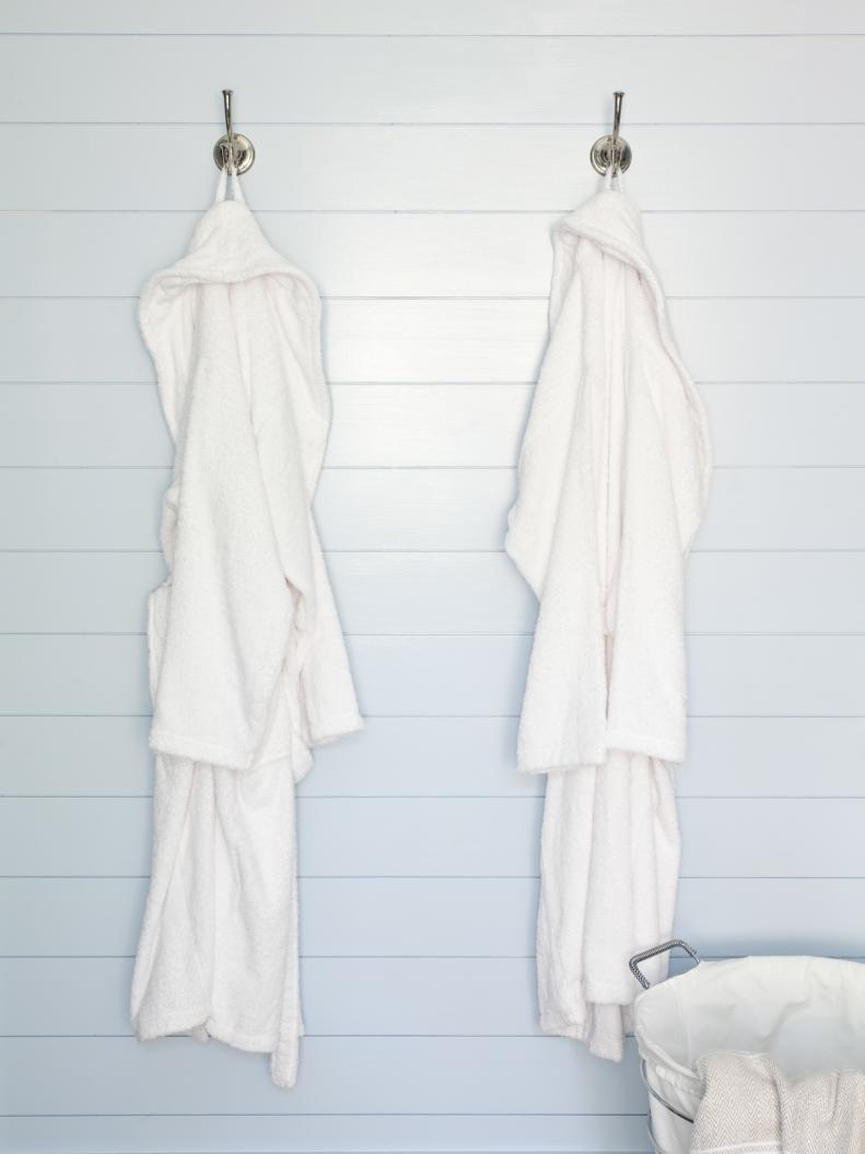 A pair of stylish robe hooks on the master bathroom wall offer hanging storage for these white terry cotton robes and other bath necessities. A wire and canvas hamper keeps dirty towels and used robes off the floor and ready for the laundry room next door.