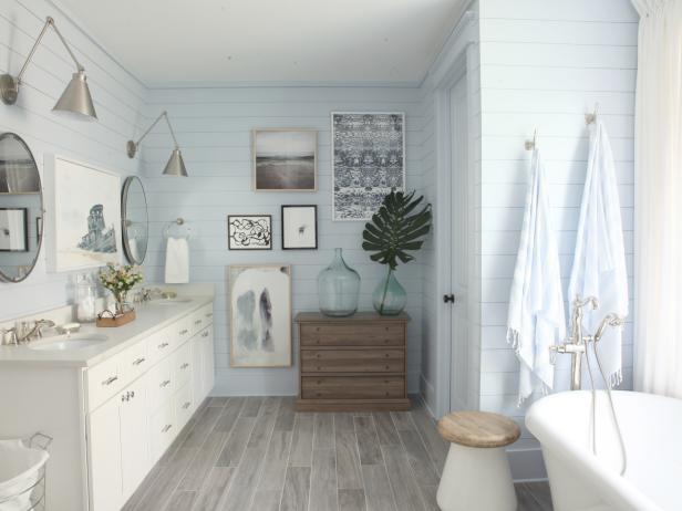 This wide view from the shower shows the weathered wood three-drawer chest with large glass jugs on top for a touch of greenery surrounded by framed art located to the left of the toilet closet.