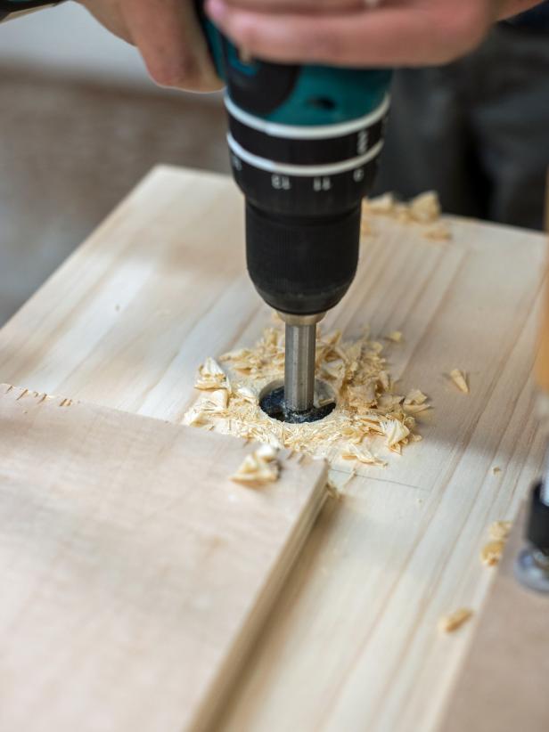 Use measuring tape to determine center point of stool top. For a 3” wide handle, measure and mark 1 ½” out length-wise from center point to the left and right. Use ½” forstner bit affixed to a drill to drill a hole just to the inside of both of those marks. Use a jig saw to cut between the two holes, completing the handle cut out.